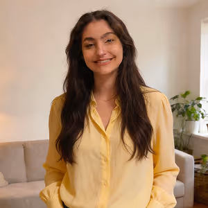 Smiling woman with long dark hair wearing a yellow blouse in a cozy living room.