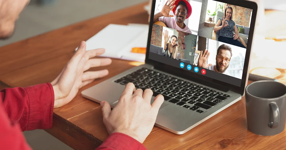 Person in red shirt uses a laptop for a video call with four people, all smiling and waving, creating a friendly and engaging virtual meeting atmosphere.