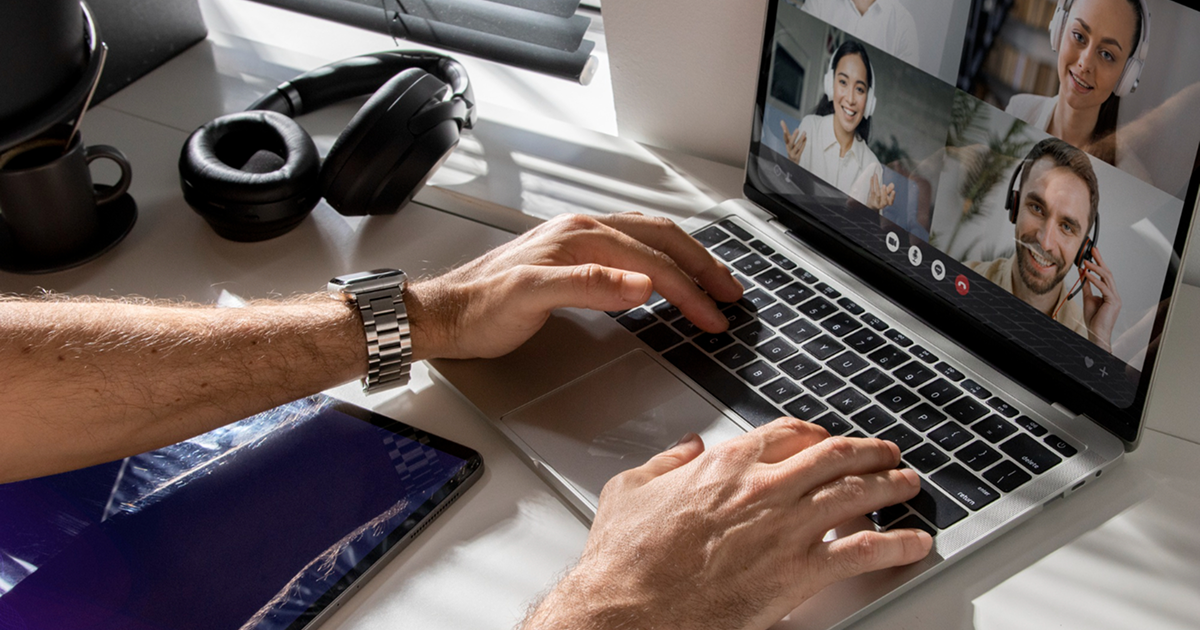 Person uses a laptop for a video call with four people, all smiling and waving, creating a friendly and engaging virtual meeting atmosphere.