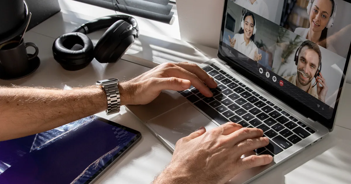 Person uses a laptop for a video call with four people, all smiling and waving, creating a friendly and engaging virtual meeting atmosphere.