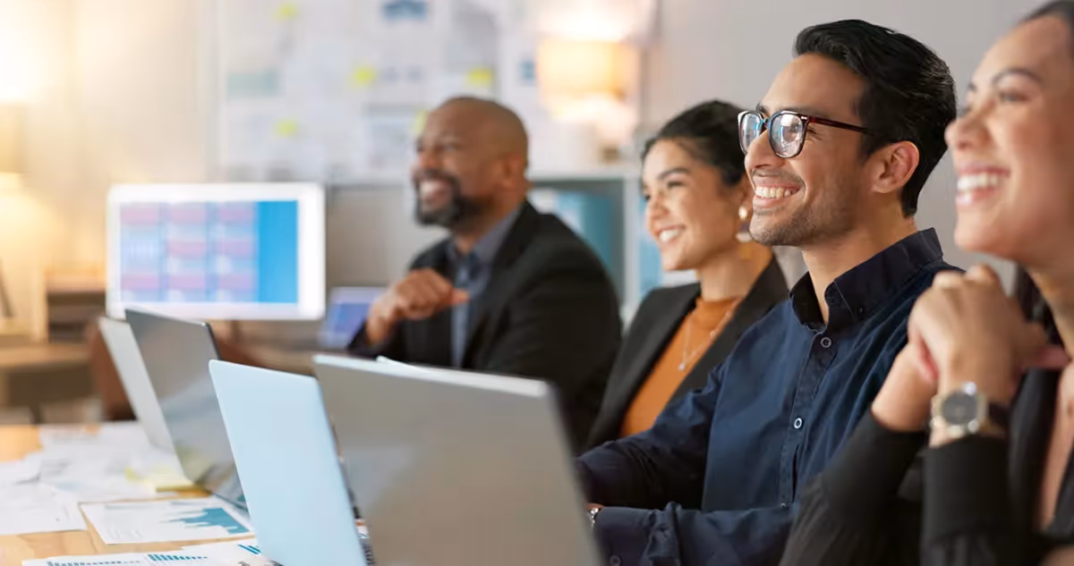 A group of diverse individuals seated at a table, each using a laptop for collaborative work or discussion.