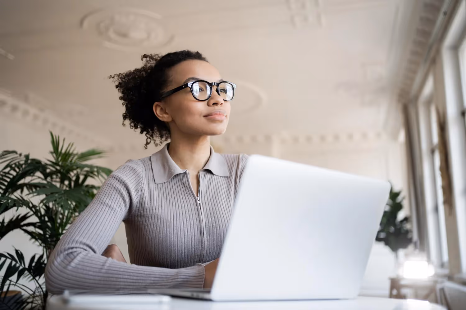 A woman wearing glasses is seated at a desk, working on a laptop.