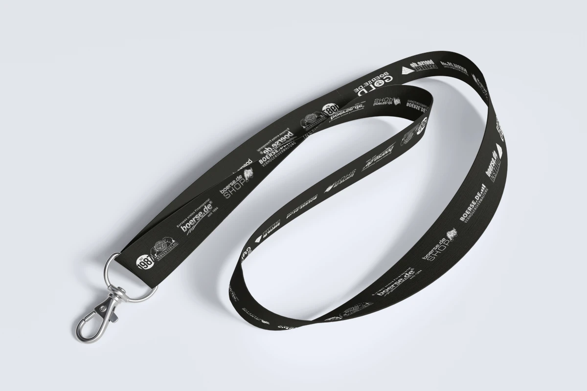 Schwarzes Schlüsselband mit weißem Text und Logos, inklusive Metallclip. Entlang der Länge erscheinen verschiedene Markennamen und Grafiken auf hellgrauem Hintergrund.