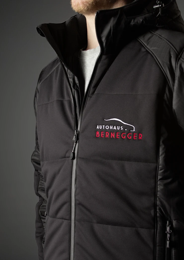Mann trägt eine schwarze Softshelljacke mit aufgesticktem Firmenlogo "Autohaus Bernegger". Dunkle, mystische Stimmung