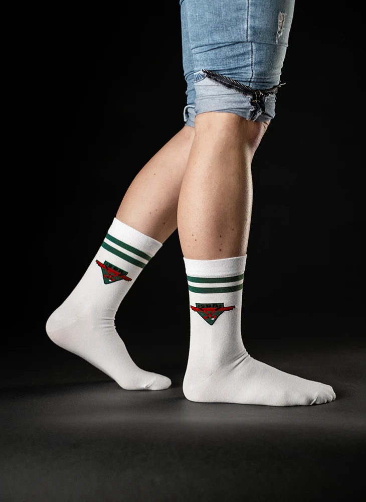 Weiße Socken mit grünen Streifen und rotem Logo. Getragen an einem stehenden Bein, das in einer kurzen Jeansshorts sichtbar ist.