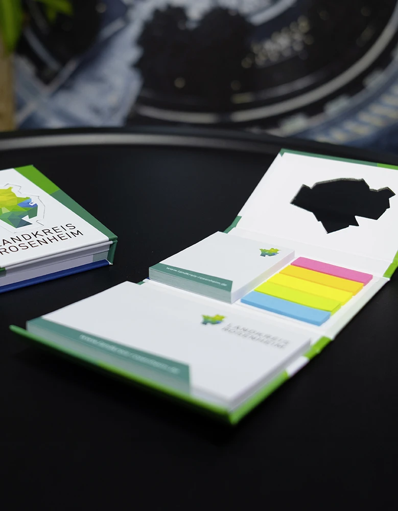 Ein Set Haftnotizen mit einem grünen und blauen Logo des Landkreises Rosenheim. Enthält bunte Haftnotizen in Gelb, Pink, Blau und Grün sowie ein Notizblock.
