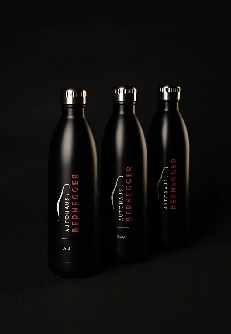 Drei schwarze Trinkflaschen aus Edelstahl mit Schraubverschluss. Auf jeder Flasche steht 'AUTOHAUS BERNEGGER' und ein Name: 'Uschi', 'Sieg'.