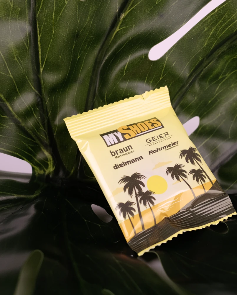 Gelbe Verpackung mit dem Text 'MY SHOES' und Abbildungen von Palmen, auf einem großen Blatt platziert.