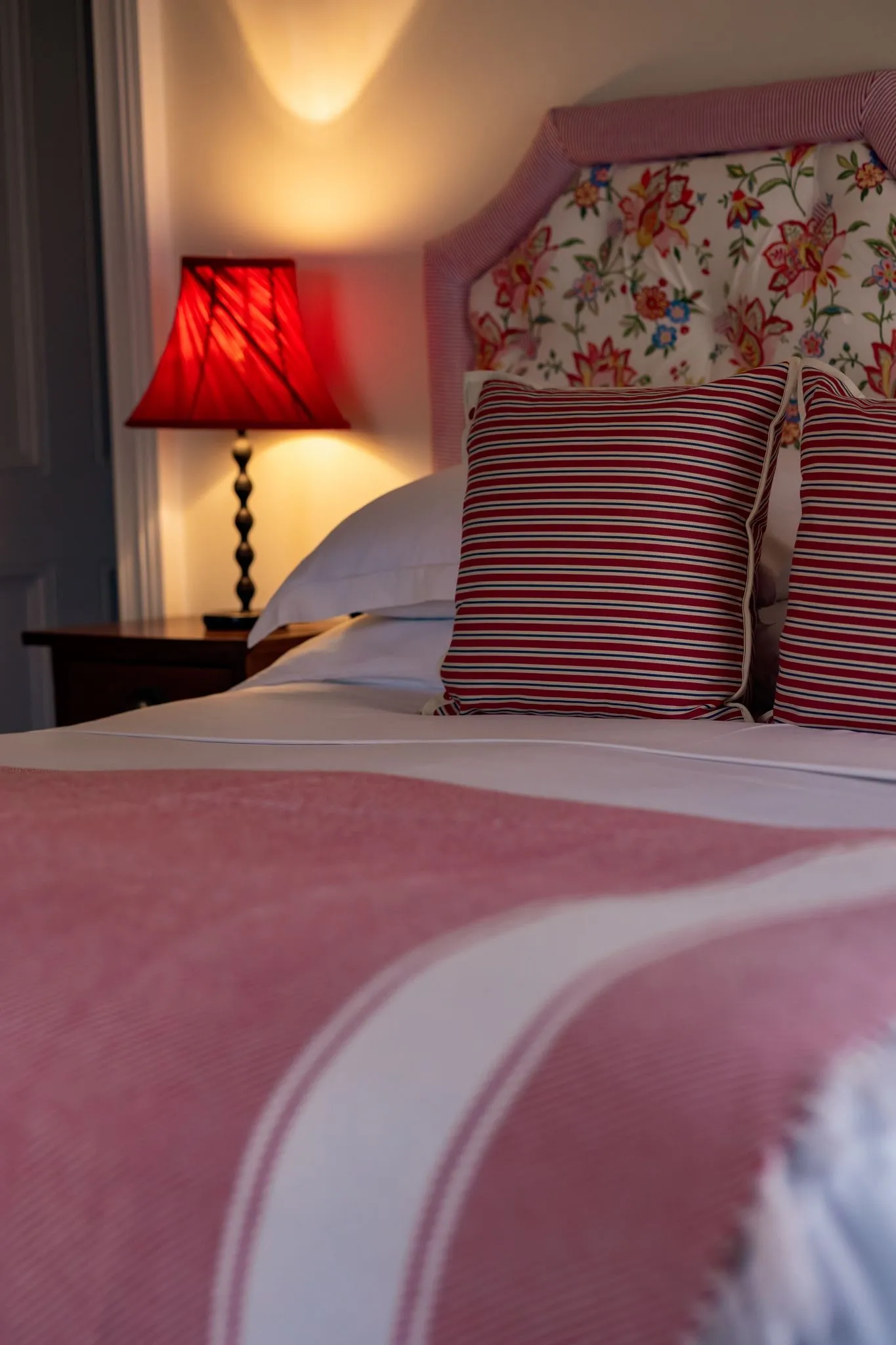 Bed with red and white striped pillows, floral headboard, red bedside lamp, and a red and white blanket.