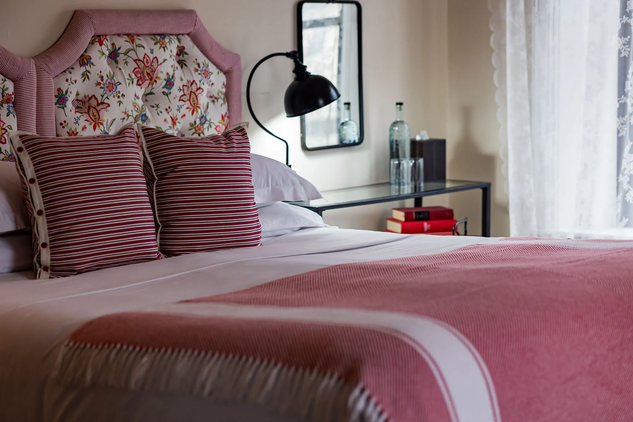 Bed with floral and striped pillows, pink headboard, and pink blanket in a softly lit bedroom.