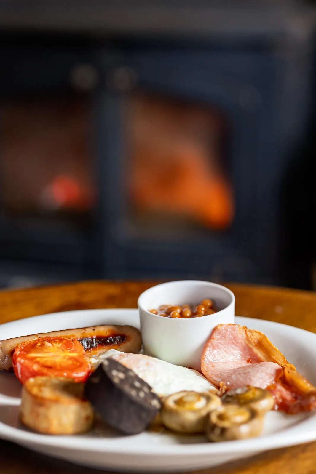 Plate of cooked English breakfast with eggs, sausage, bacon, tomato, mushrooms, black pudding, and beans.
