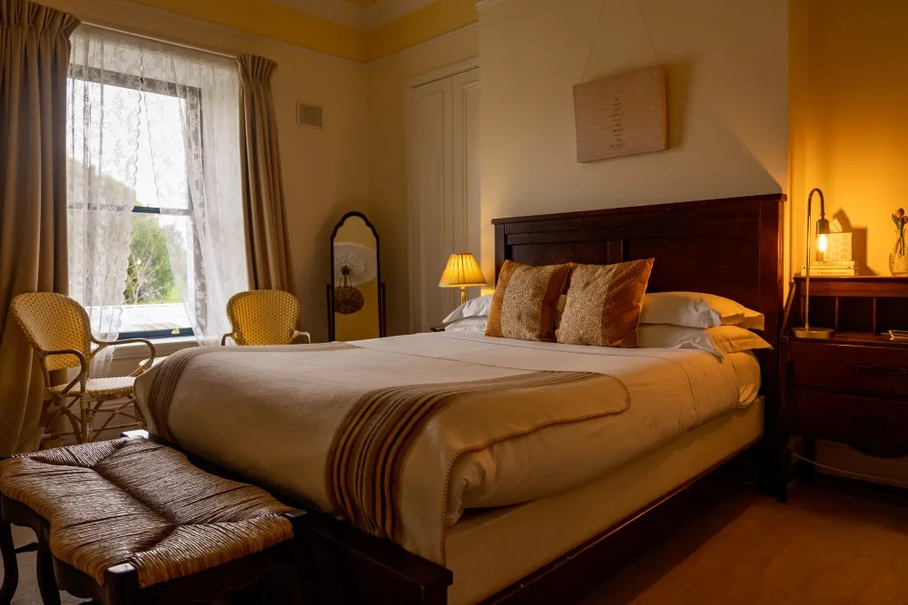 Cozy bedroom with a large bed, wooden headboard, two decorative pillows, and warm lighting.