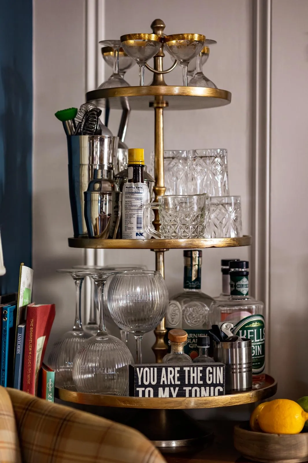 Three-tiered gold bar cart with glassware, gin bottles, bar tools, and a sign reading 'You are the gin to my tonic'.