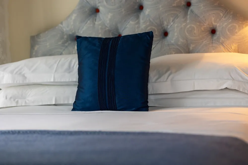 Close-up of a neatly made bed with white linens, a navy blue decorative pillow, and a patterned headboard.