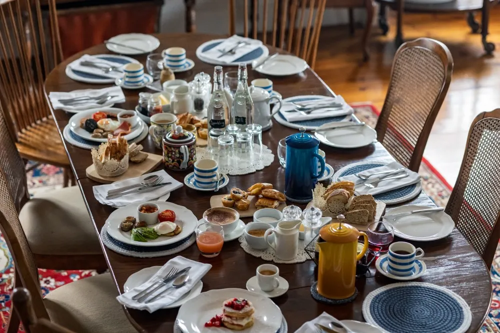 Wooden dining table set for breakfast with plates of food, coffee pots, juice, and cups.