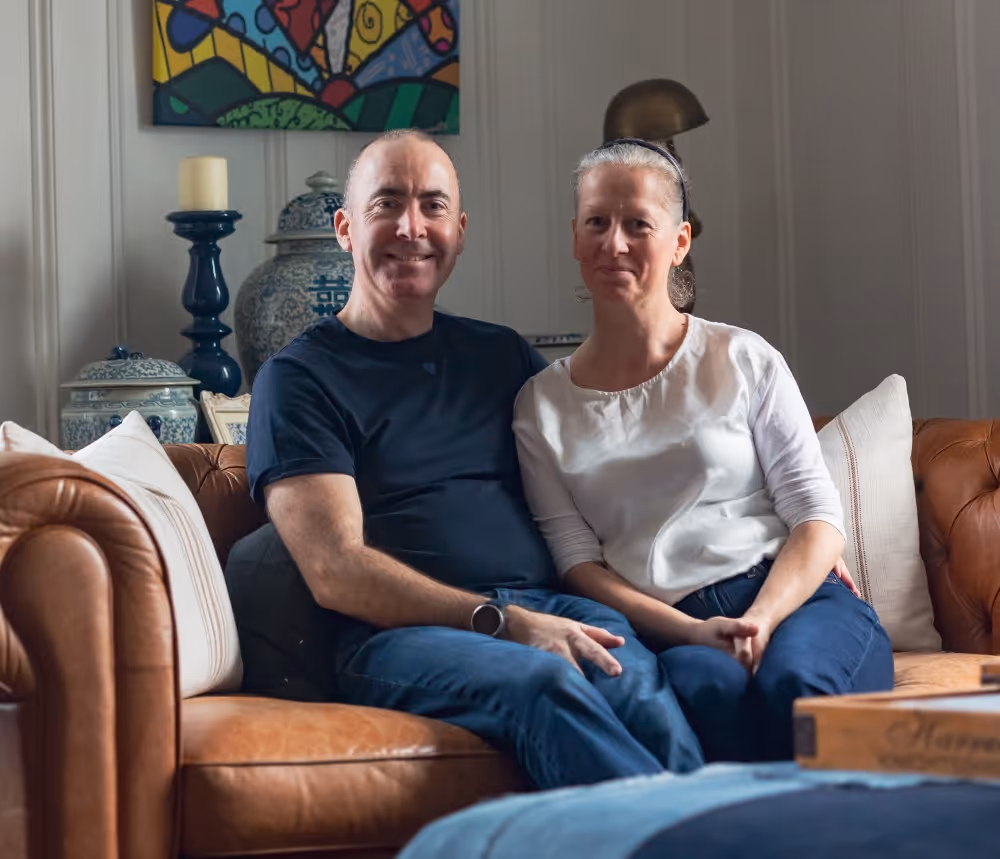 Smiling couple sitting close on a brown leather couch in a cozy living room.