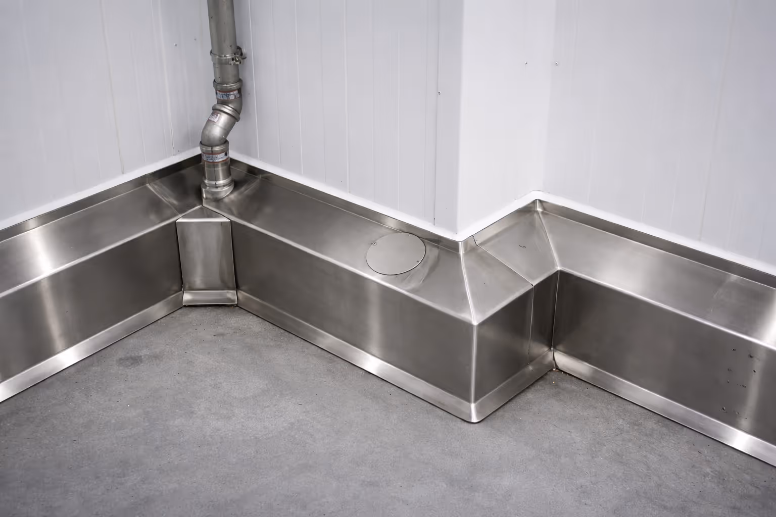 Corner of a clean industrial room with stainless steel baseboards and a metal pipe running down the wall.