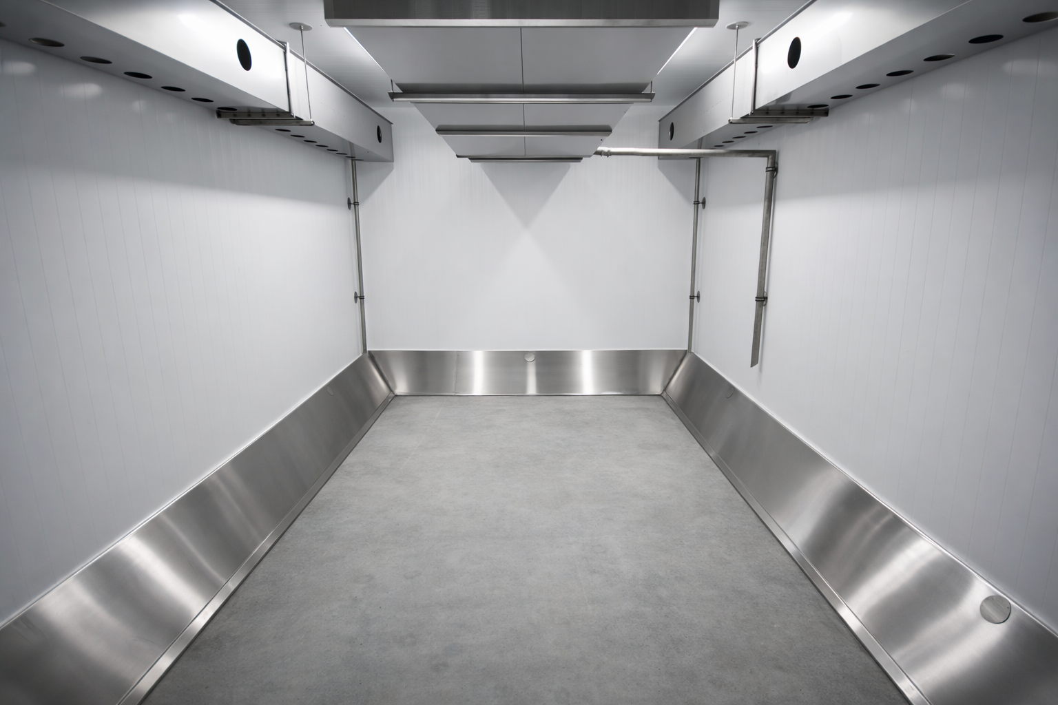 Empty industrial room with white walls, stainless steel skirting, and overhead ventilation ducts.