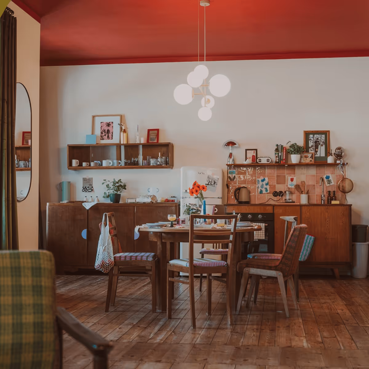 Wnętrze przytulnego apartamentu w stylu PRL, stół z krzesłami, drewniana podłoga i komoda – Slowhop