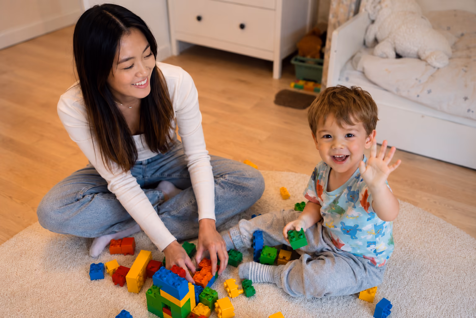 Babysitter and a child play with colorful building blocks on an indoor carpet.