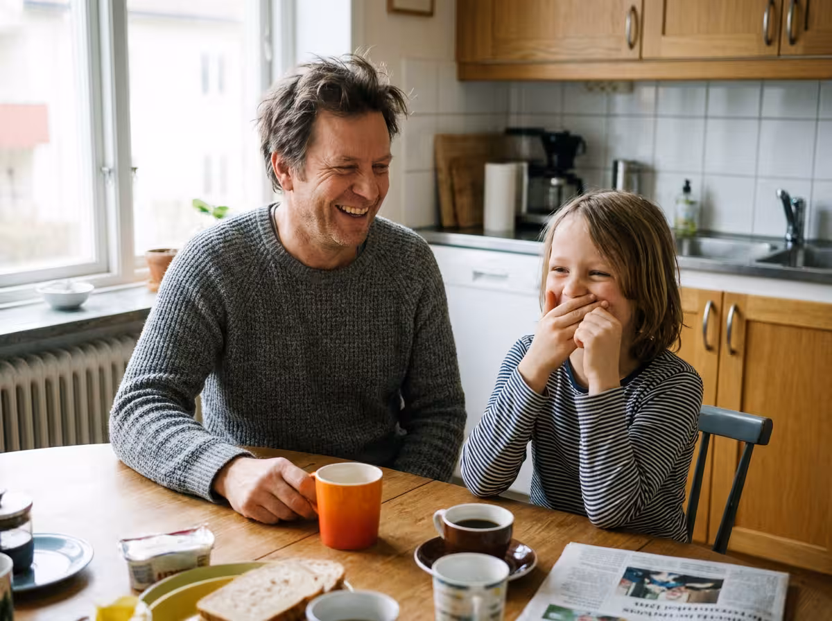 Pappa och barn skrattar tillsammans vid köksbordet efter ett pappaskämt