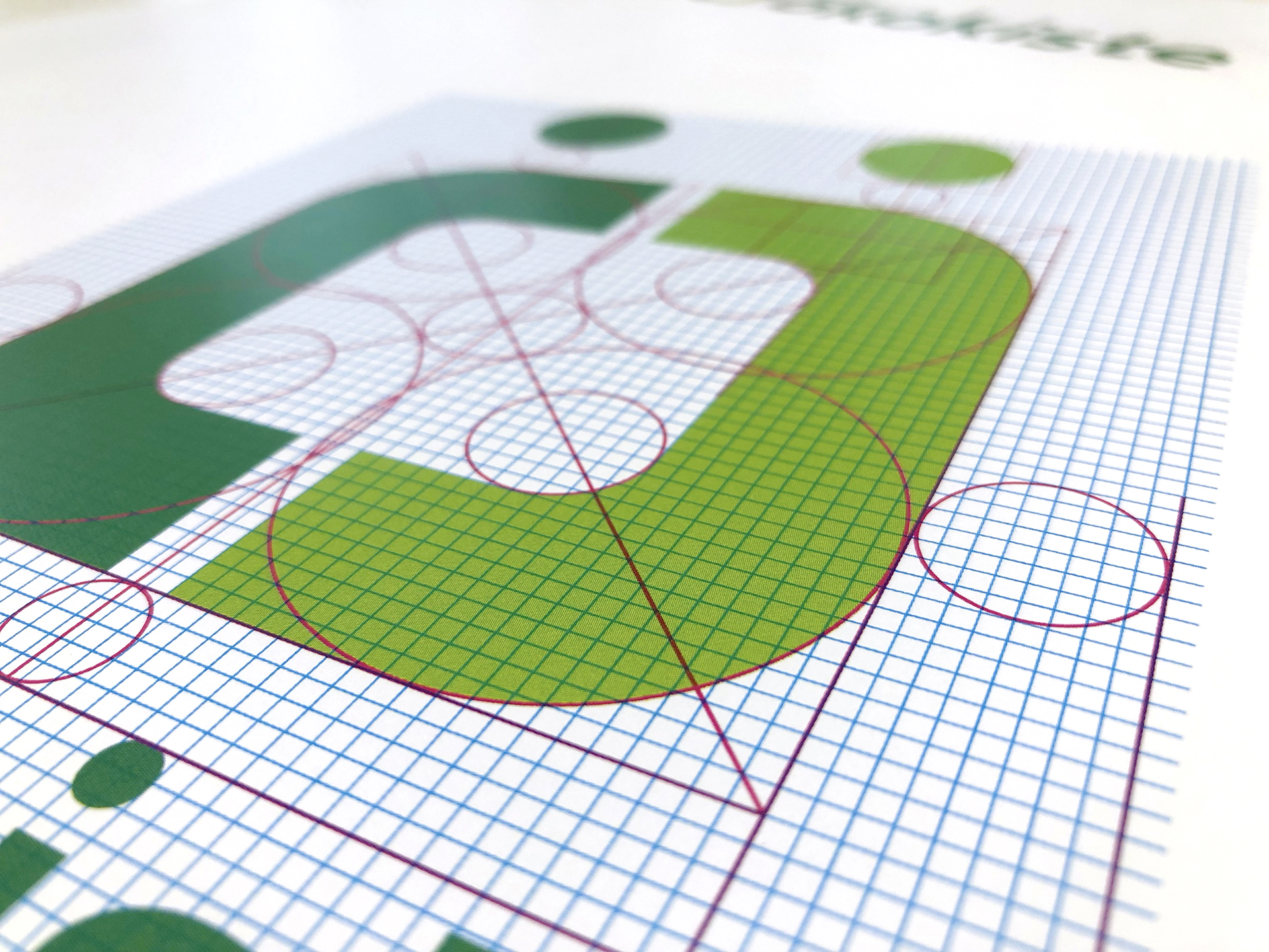 Nahaufnahme eines grafischen Designs mit grünen geometrischen Formen und runden Ecken auf kariertem Papier, überlagert von roten und blauen Hilfslinien und Kreisen.