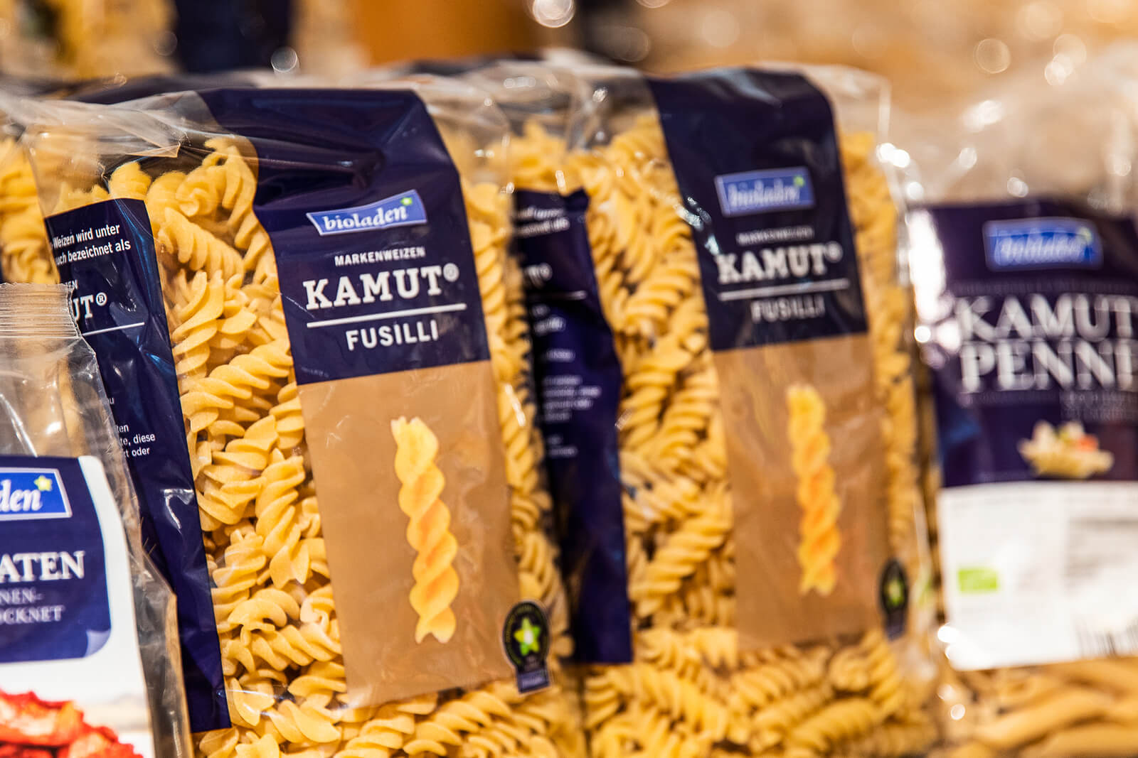 Mehrere Packungen Bioladen Kamut Fusilli Nudeln aus Hartweizengrieß stehen nebeneinander, die Spiralförmigen Nudeln sind sichtbar durch die transparente Verpackung.
