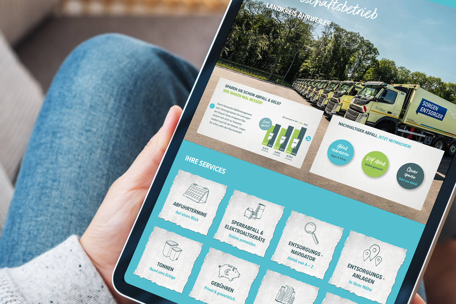 Person hält ein Tablet, auf dem eine Webseite für Abfallentsorgung angezeigt wird mit Bildreihe von Müllfahrzeugen, einem Diagramm zum Abfallmanagement, Tipps für nachhaltigen Abfall sowie Serviceoptionen wie Abfuhrtermine, Sperrabfall und Elektrogeräte, Tonnen, Gebühren, Entsorgungsnavigator und -anlagen.