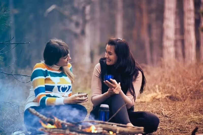 deux femmes qui discutent assises dans la forêt autour d'un feu de joie