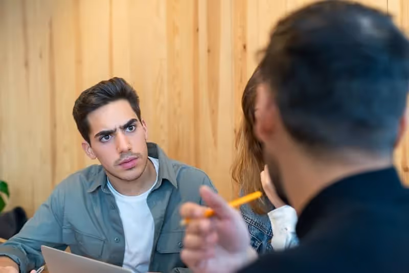 Jeune étudiant homme étonné qui essaie de comprendre quelque chose qu'un autre étudiant lui explique