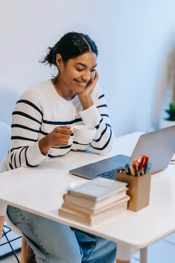 jeune femme souriant en face de son ordinateur portale avec une tasse de café à la main