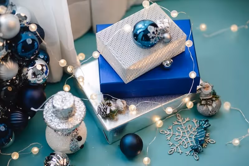 cadeaux de Noël emballés en bleu et argentés et posé sur un support bleu avec des décorations de Noël et des luminaires