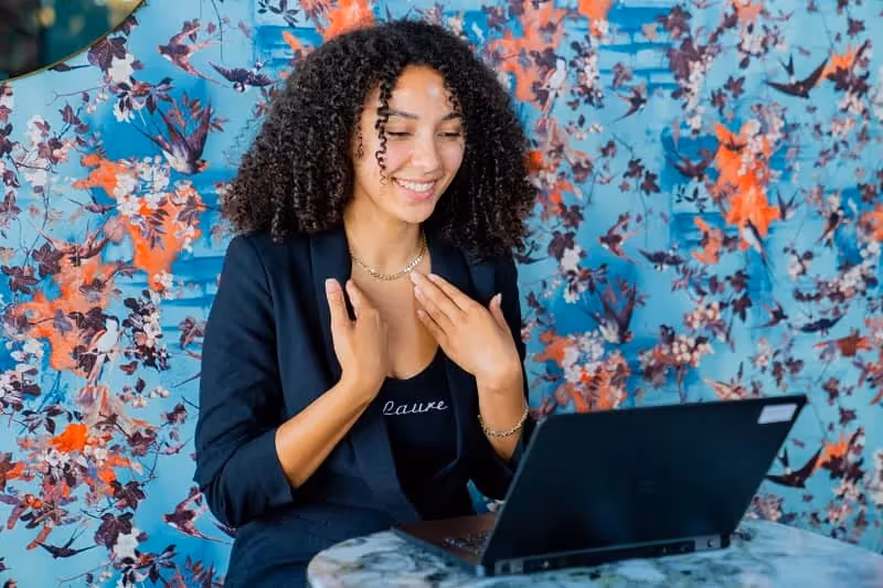 Femme aux cheveux bouclés souriante face à son ordinateur
