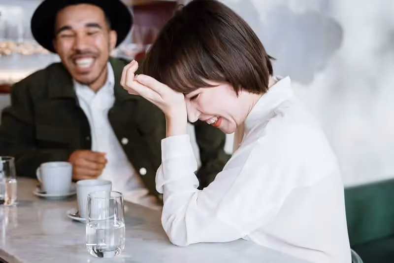 femme et hommes qui rient à une blague en prenant un café