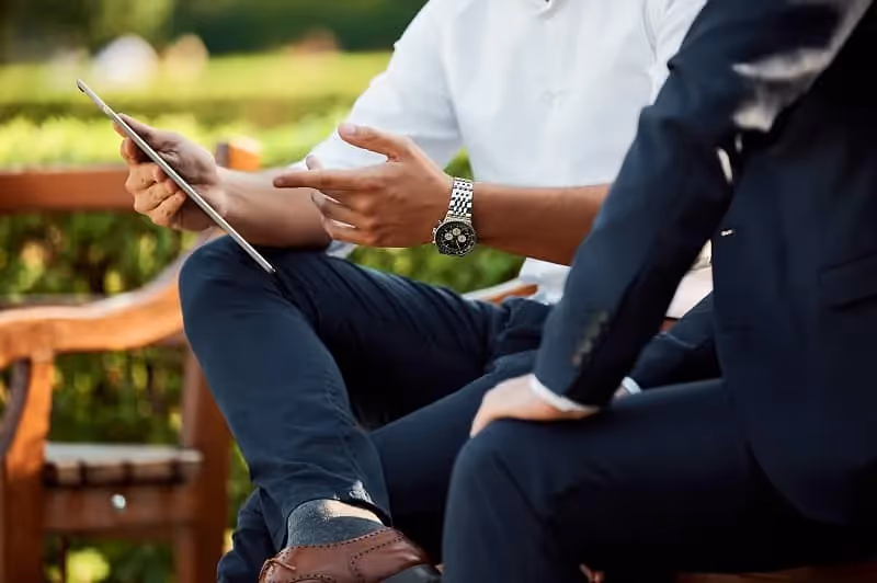 deux hommes qui négocient assis sur un banc dehors dans un parcc