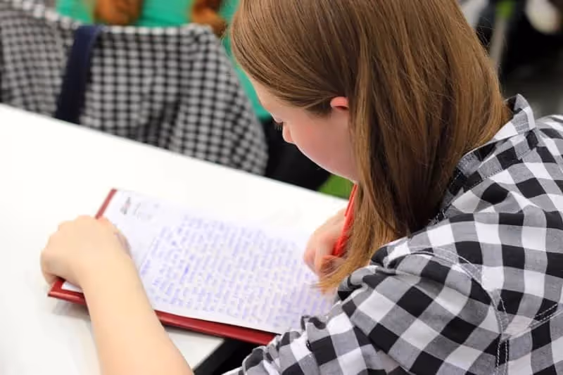 Jeune femme blonde qui écrit sur un une feuille en salle de classe