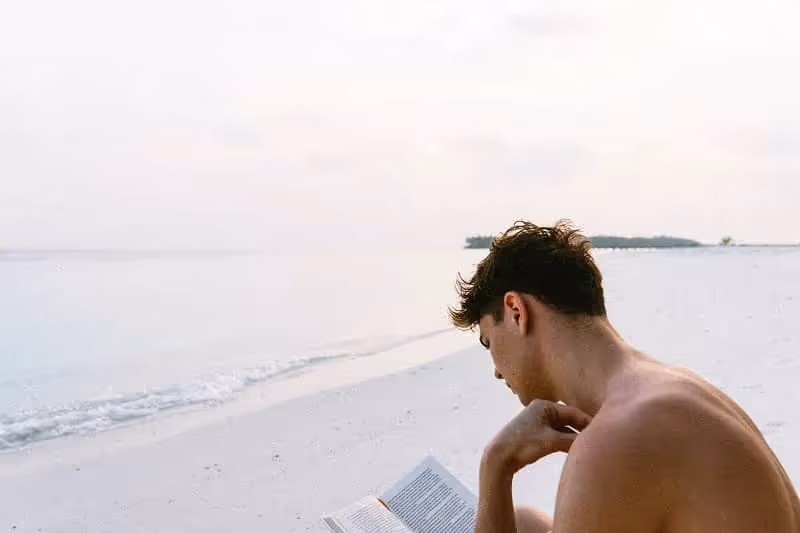 jeune homme qui lit un livre au bord de la mer