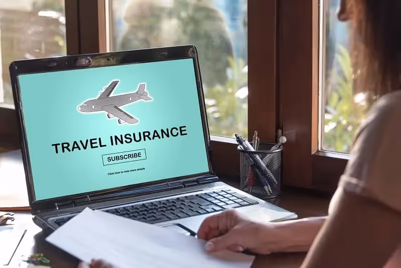 femme devant son ordinateur portable avec un écran montrant écrit "travel insurance" en anglais avec un avion et fond vert