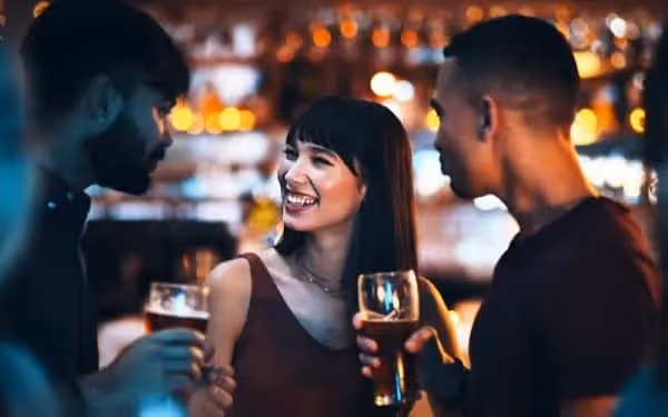 Une femme qui prend des nouvelle de deux de ses amis en prenant un verre avec eux dans un bar le soir