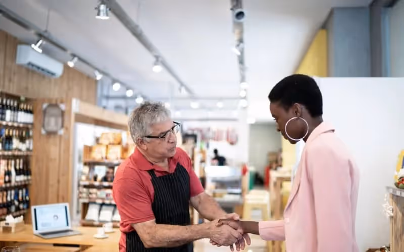 Homme âgé qui travaille dans une épicerie et accueille une cliente