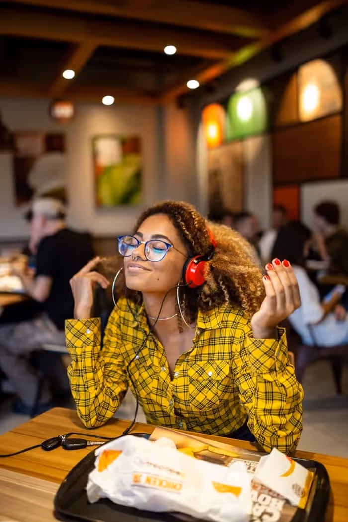 Femme avec lunette de vues noires assise dans un café tout en écoutant de la musique anglais avec son casque
