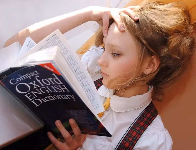 Fille blonde concentrée qui lit un livre sur la grammaire anglaise notamment sur le génitif en anglais