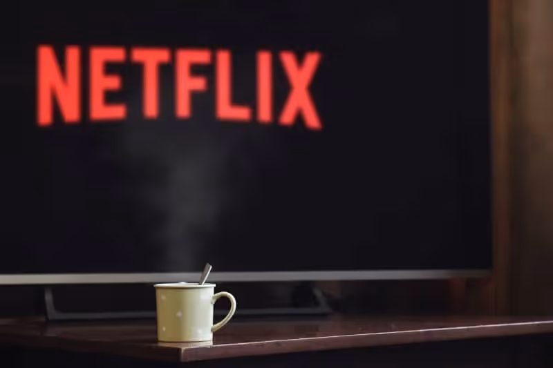 écran de télévision affichant Netfliw avec une tasse jaune posée sur une table basse devant la télévision