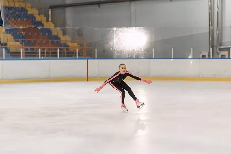 jeune fille habillée de noir et rose qui fait du patinage artistique dans une patinoire vide