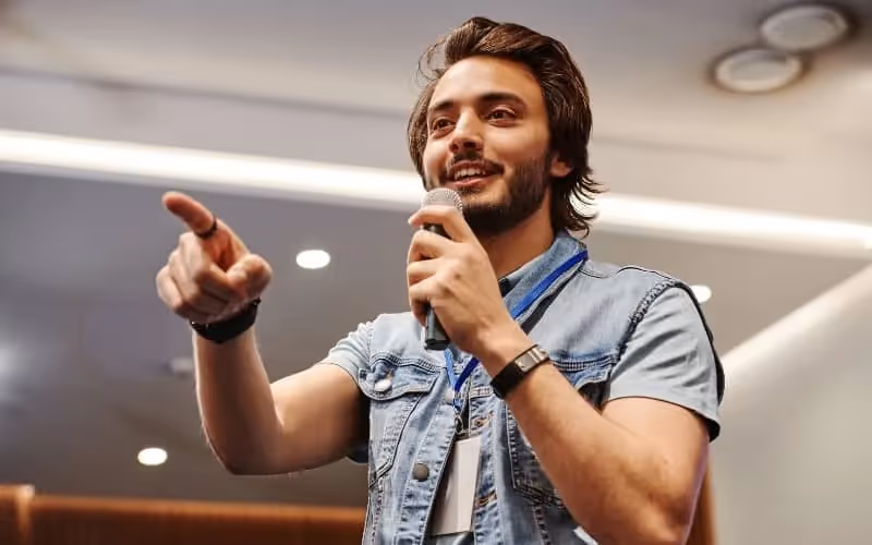 homme qui parle dans micro en pointant quelqu'un du doigt