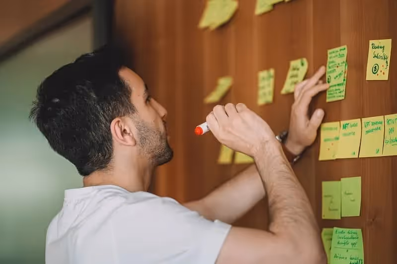 jeune homme qui colle des stickers jaunes sur un mur et qui écrit dessussur ces
