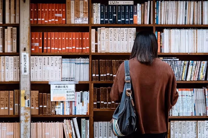 femme à la bibliothèque qui cherche un livre sur le past simple