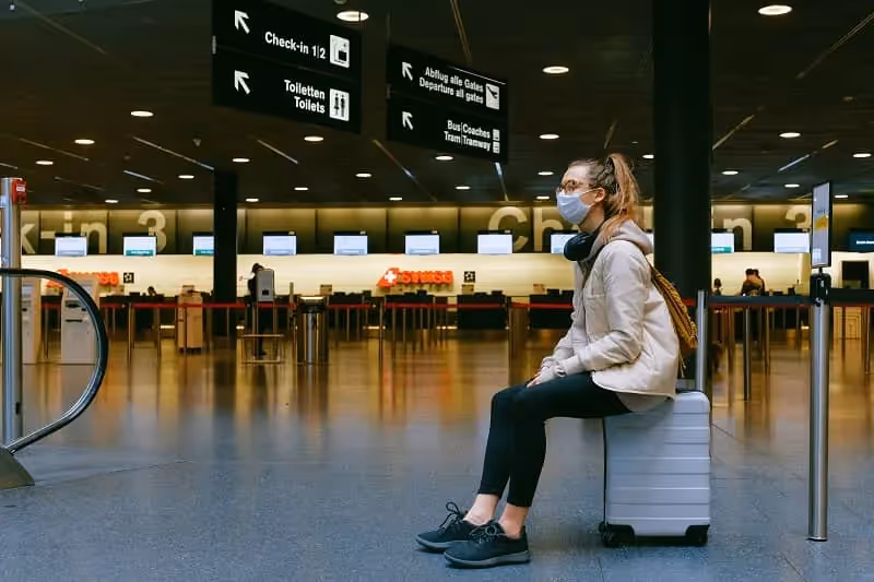 femme assise sur sa valise au milieu de l'aéroport en pleine saison de pandémie