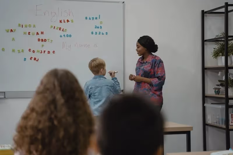 salle de classe de langue anglaise avec élève blond au tableau qui apprend à écrire son prénom en anglais