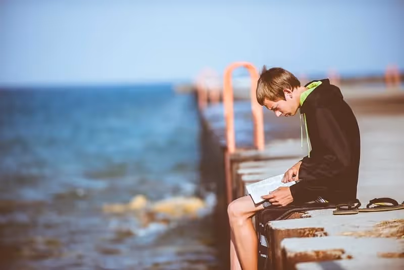 jeune garçon qui lit un livre au bord de mer